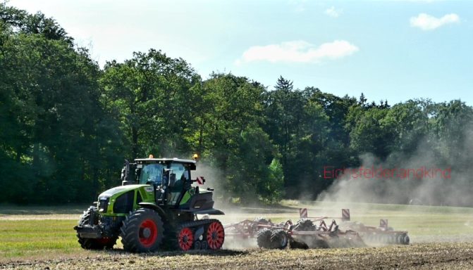 Ein Traktor pflügt einen Feldabschnitt, umgeben von Bäumen und leichtem Staub.